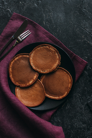 top view of plate of chocolate pancakes with cutlery on red napkin