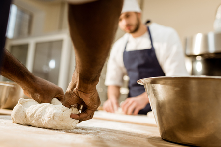cropped shot of bakers kneading dough together at baking manufactureの写真素材