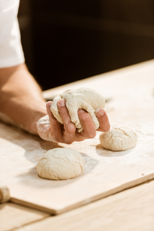 cropped shot of baker kneading dough for pastry on messy tableの写真素材