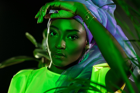 beautiful african american woman in traditional wire head wrap under green light behind leavesの写真素材