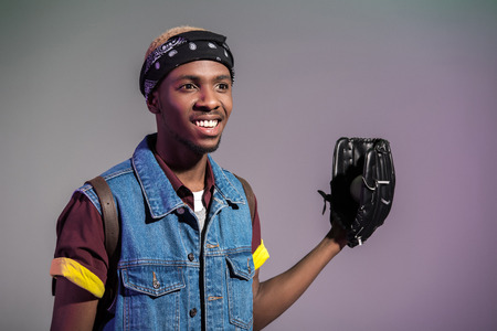 smiling young african american man with baseball glove looking away isolated on grey