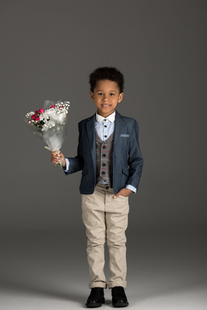 smiling african american kid standing with bouquet of flowers on grayの写真素材