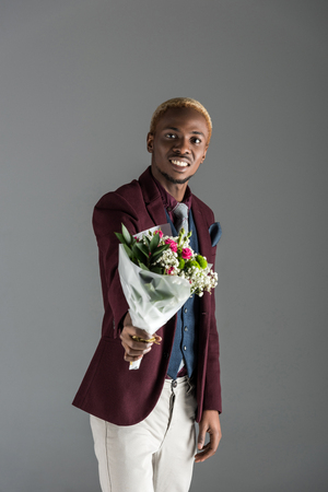 smiling african american man with bouquet in hand isolated on greyの写真素材
