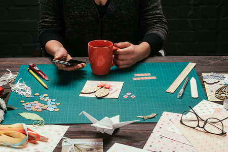 cropped image of woman sitting and holding smartphone and cup of coffee in handsの写真素材