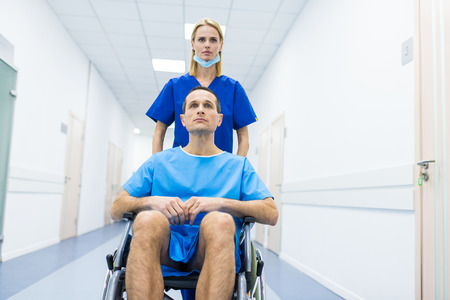 female surgeon and male patient in wheelchair in hospital corridorの写真素材