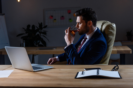 businessman sitting in dark office and drinking whiskeyの写真素材