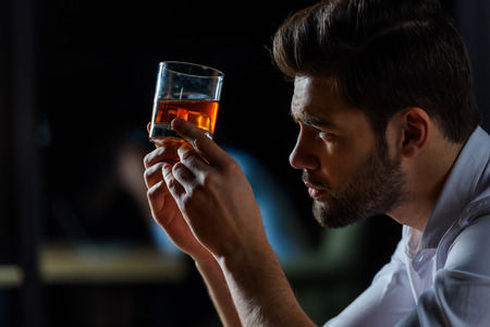 side view of handsome businessman looking at glass of whiskeyの写真素材