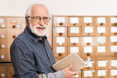 smiling senior male archivist holding book and looking at camera