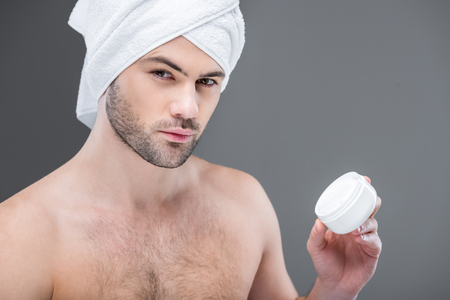 bearded man in towel holding face cream, isolated on greyの写真素材