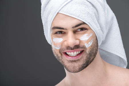 smiling man in towel with cream on face, isolated on greyの写真素材