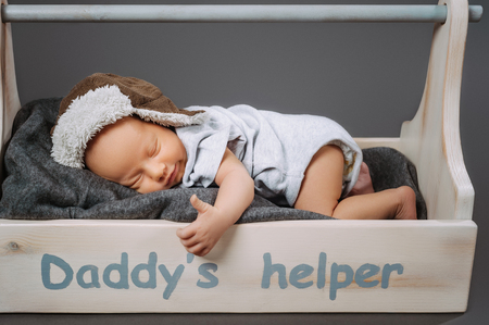 cute infant baby showing thumb up while sleeping in wooden toolbox with daddys helper letteringの写真素材