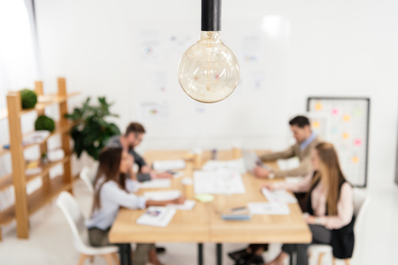 selective focus of light bulb and multicultural group of marketing managers working in officeの写真素材