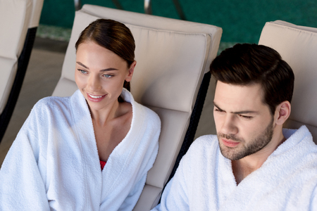 happy young couple in bathrobes smiling and looking away in spa centerの写真素材