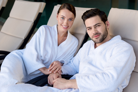 happy young couple in bathrobes smiling and camera in spa centerの写真素材