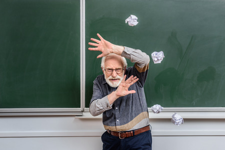 senior lecturer protecting himself of falling crumpled pieces of paperの写真素材