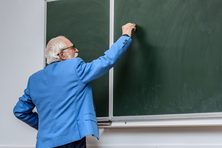 rear view of senior lecturer writing something on blackboard with piece of chalkの写真素材