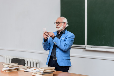 grey hair professor looking at smartphone in lecture roomの写真素材