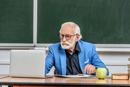 grey hair professor using laptop at table in lecture hall