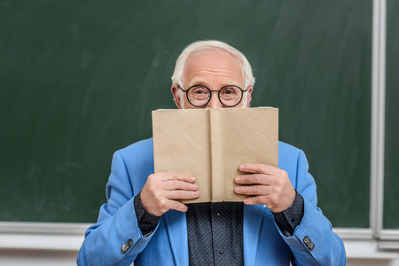 grey hair professor looking out from book