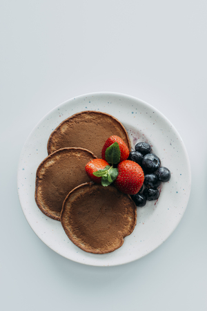 top view of chocolate pancakes with berries on white tableの写真素材