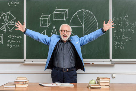 happy senior lecturer with open arms standing near blackboardの写真素材