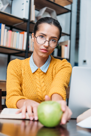 young student girl preparing for exam at library and holding green appleの写真素材