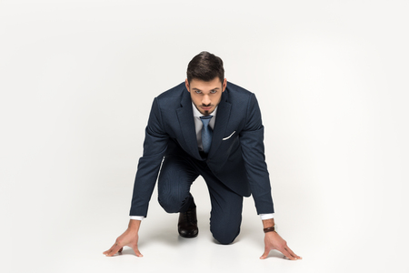 serious young businessman in starting position ready to run isolated on greyの写真素材