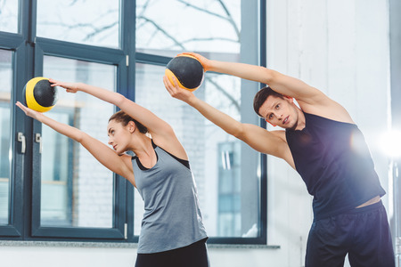 sporty young couple holding balls and training together in gym