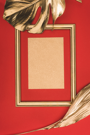 top view of golden photo frame, leaves and blank paper isolated on redの写真素材