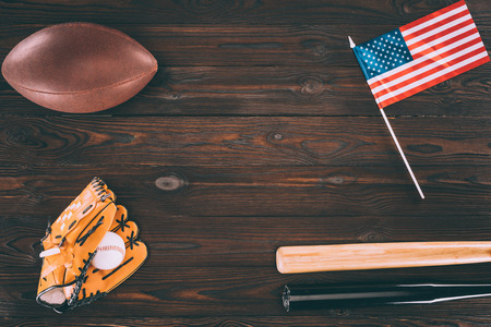 top view of us flag, rugby ball, baseball bats and glove with ball on wooden tableの写真素材