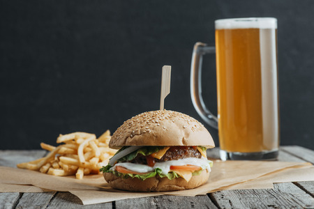 traditional homemade hamburger, french fries and glass of beer on baking paper on wooden tableの写真素材
