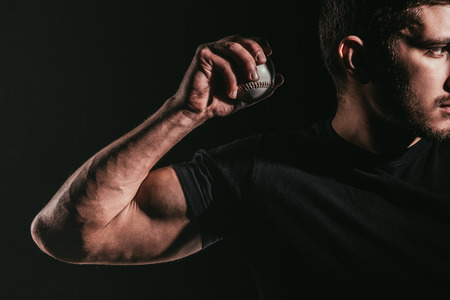 cropped shot of young muscular sportsman holding baseball ball isolated on blackの写真素材