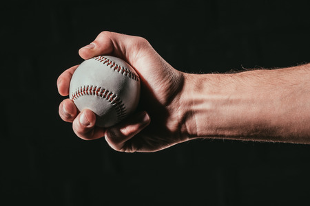 cropped shot of male hand holding baseball ball isolated on blackの写真素材