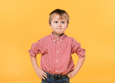 portrait of little boy in shirt standing akimbo isolated on yellow