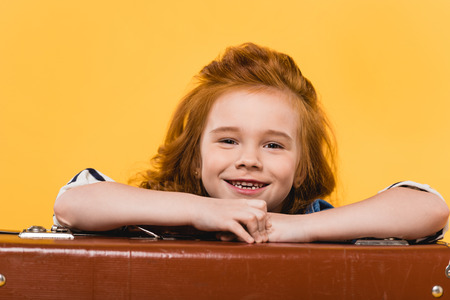 portrait of smiling kid leaning on suitcase isolated on yellowの写真素材