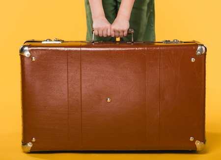 partial view of child holding leather suitcase isolated on yellowの写真素材