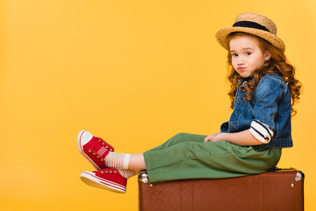 side view of kid sitting in suitcase isolated on yellowの写真素材