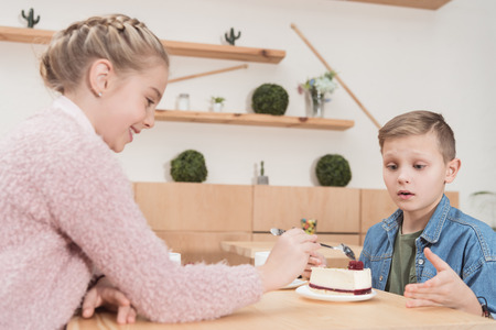 children sitting at table at cafe while looking at cake on table at cafeの写真素材