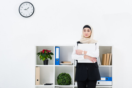 portrait of businesswoman in hijab with folder in hands in officeの写真素材