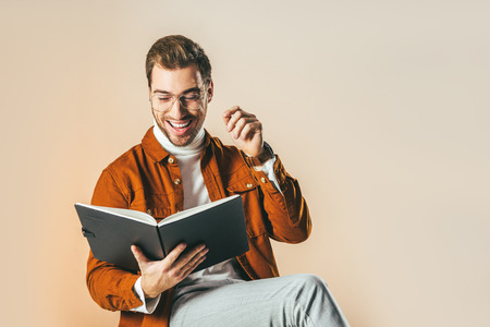 portrait of cheerful man reading notebook isolated on beige