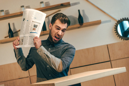 portrait of angry businessman throwing newspaper at table in cafeの写真素材