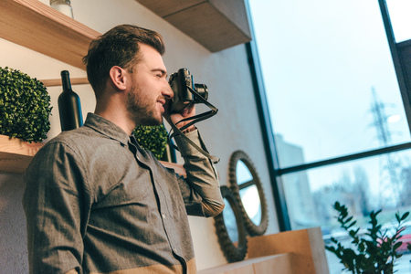 side view of smiling man taking picture on photo camera in cafeの写真素材