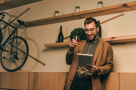 portrait of stylish man with glass of whiskey using tablet in cafeの写真素材
