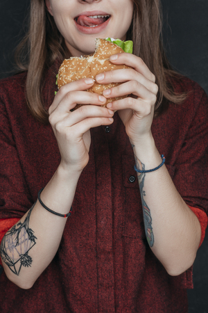 cropped view of tattooed girl eating tasty hamburgerの写真素材