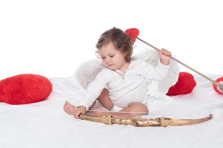 little cherub sitting on bed with bow and arrow, isolated on whiteの写真素材