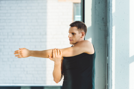 side view of young man stretching before workout in gymの写真素材