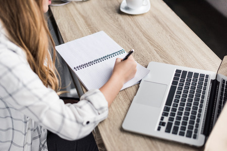 cropped shot of young woman writing in notebook at workplace