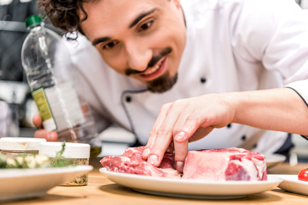 smiling chef adding oil to raw meatの写真素材