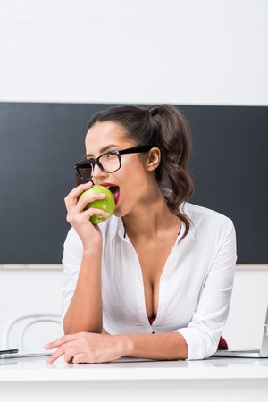 young sexy teacher eating apple at workdesk in classの写真素材