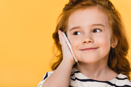 portrait of cute child talking on smartphone isolated on yellow